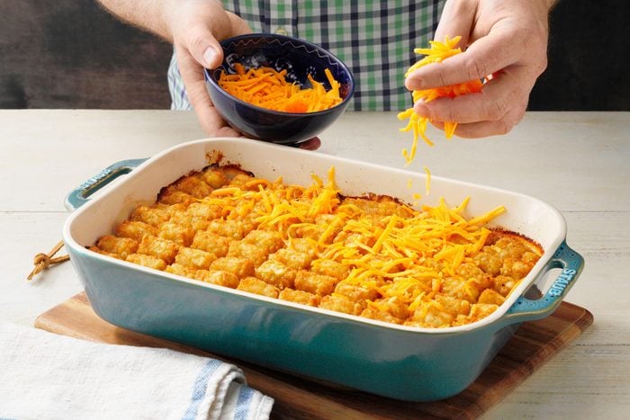 sprinkling cheese onto the baked tater tot casserole 