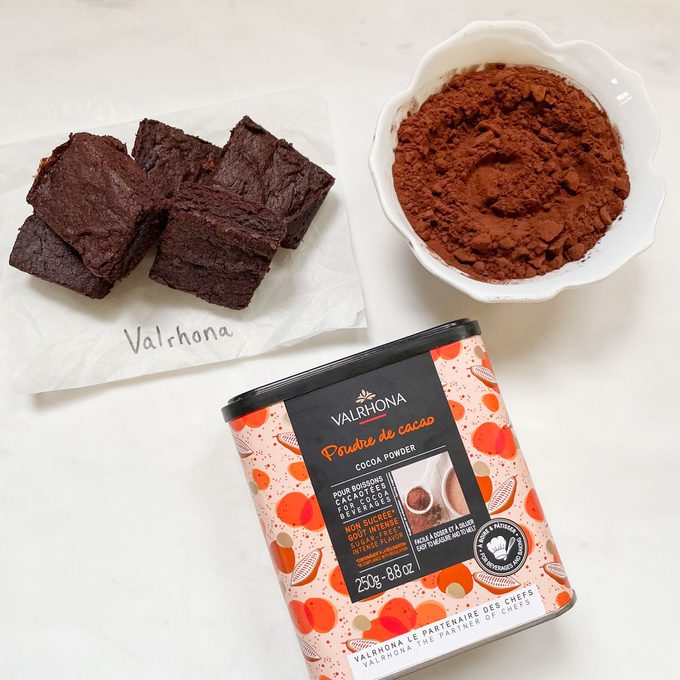Valrhona cocoa powder container, cocoa powder in a bowl, and a few brownies