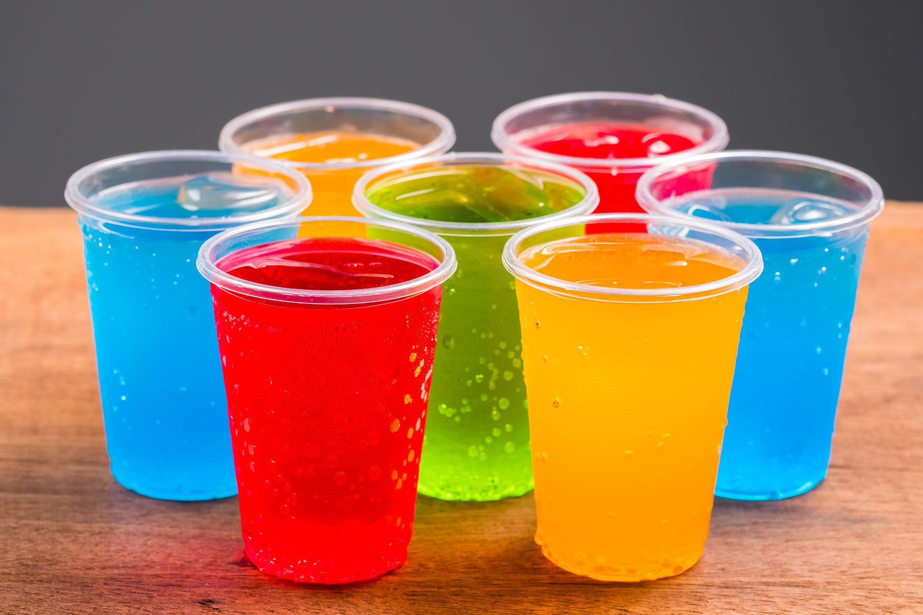 Various Colorful cold drinks in plastic cups and on a wooden and gray background