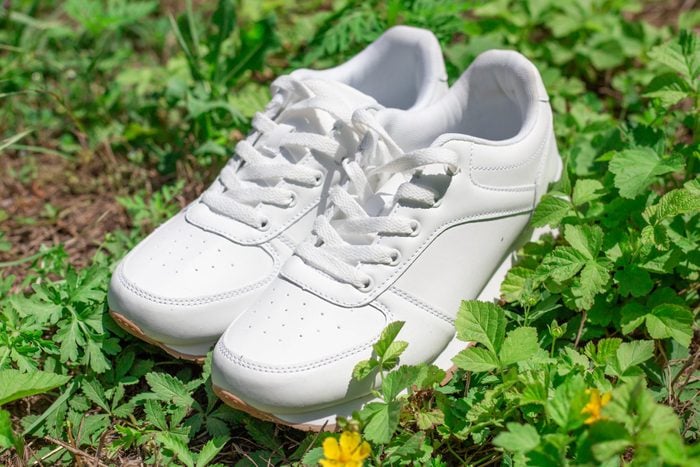 White women's sneakers stand on the green grass. Fashionable comfortable shoes for sports