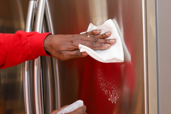 A black African-American man cleaning a stainless steel French door refrigerator in a kitchen