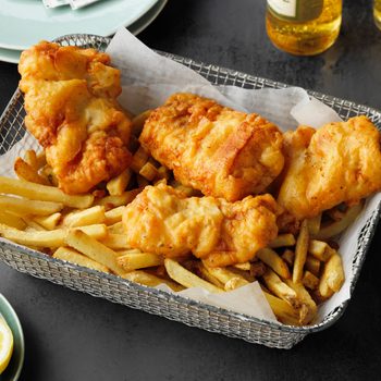 Beer Battered Fish On a Platter with french fries. glasses of beer and serving plates nearby