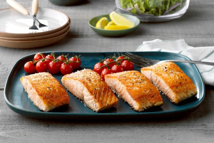 Pan-fried salmon on a blue serving platter on a gray wood table