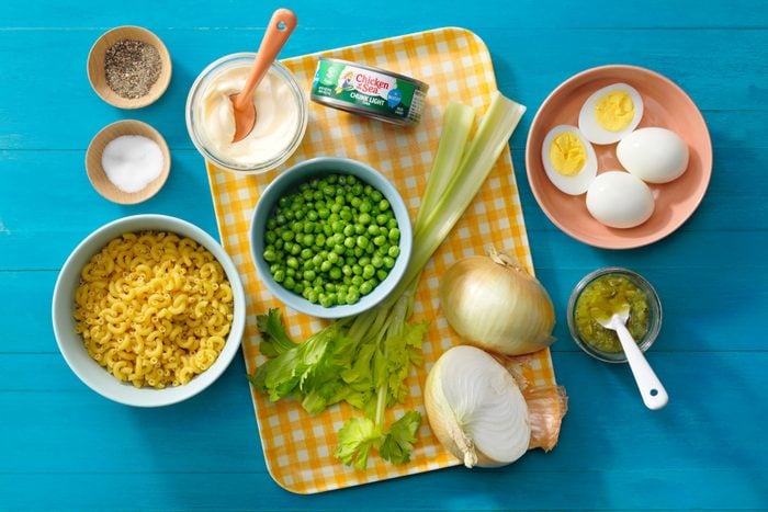 Tuna Macaroni Salad Ingredients arranged on a yellow gingham tray and colorful bowls on blue surface