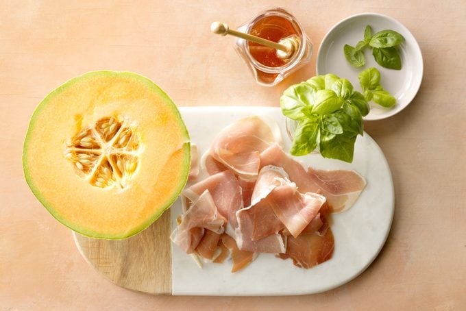 Prosciutto And Melon appetizer ingredients on peach surface