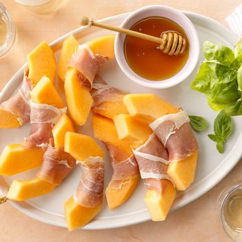 Prosciutto And Melon Appetizer arranged on a tray with honey and basil; on peach surface