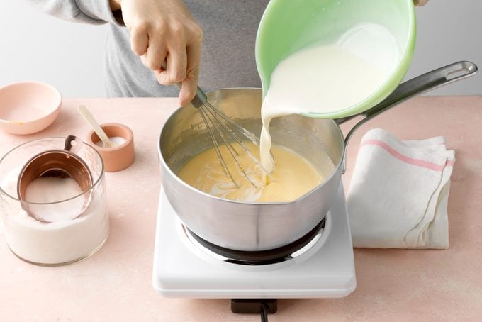 pouring cream into a pot and stirring with a whisk