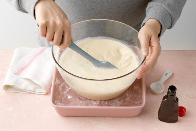 hands stirring custard in a large glass bowl making Cherry Ice Cream