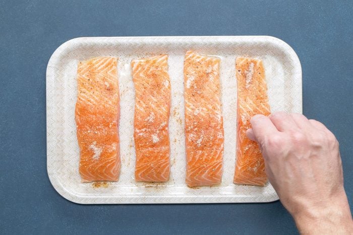 A person Sprinkling the seasoning mixture evenly on salmon fillets