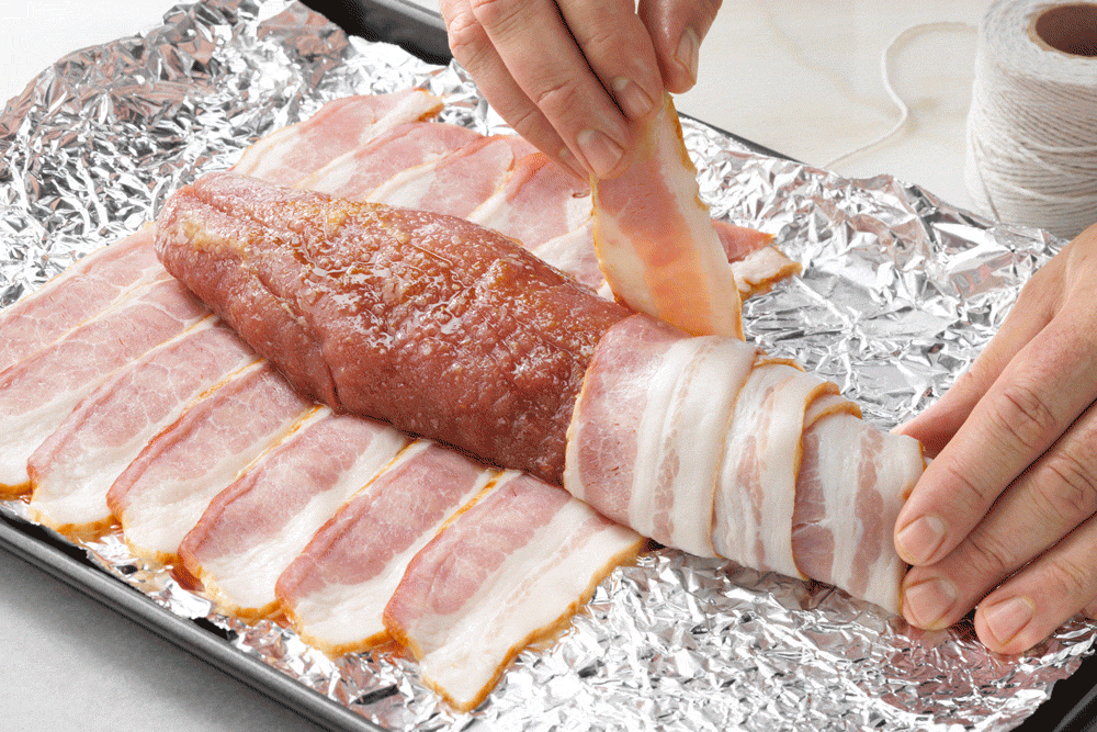 hands wrapping bacon strips around meat for Bacon Wrapped Pork Tenderloin