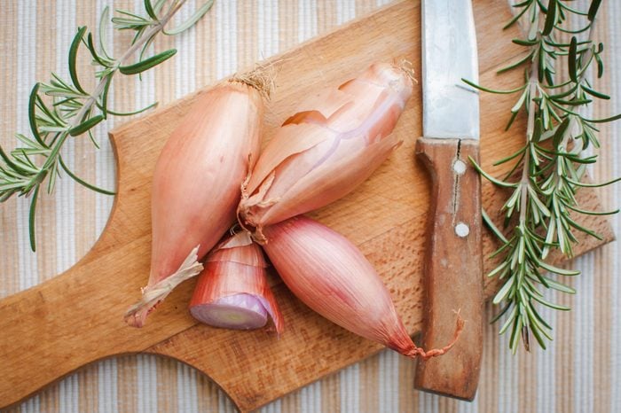 Four shallots with fresh rosemary on cutting board