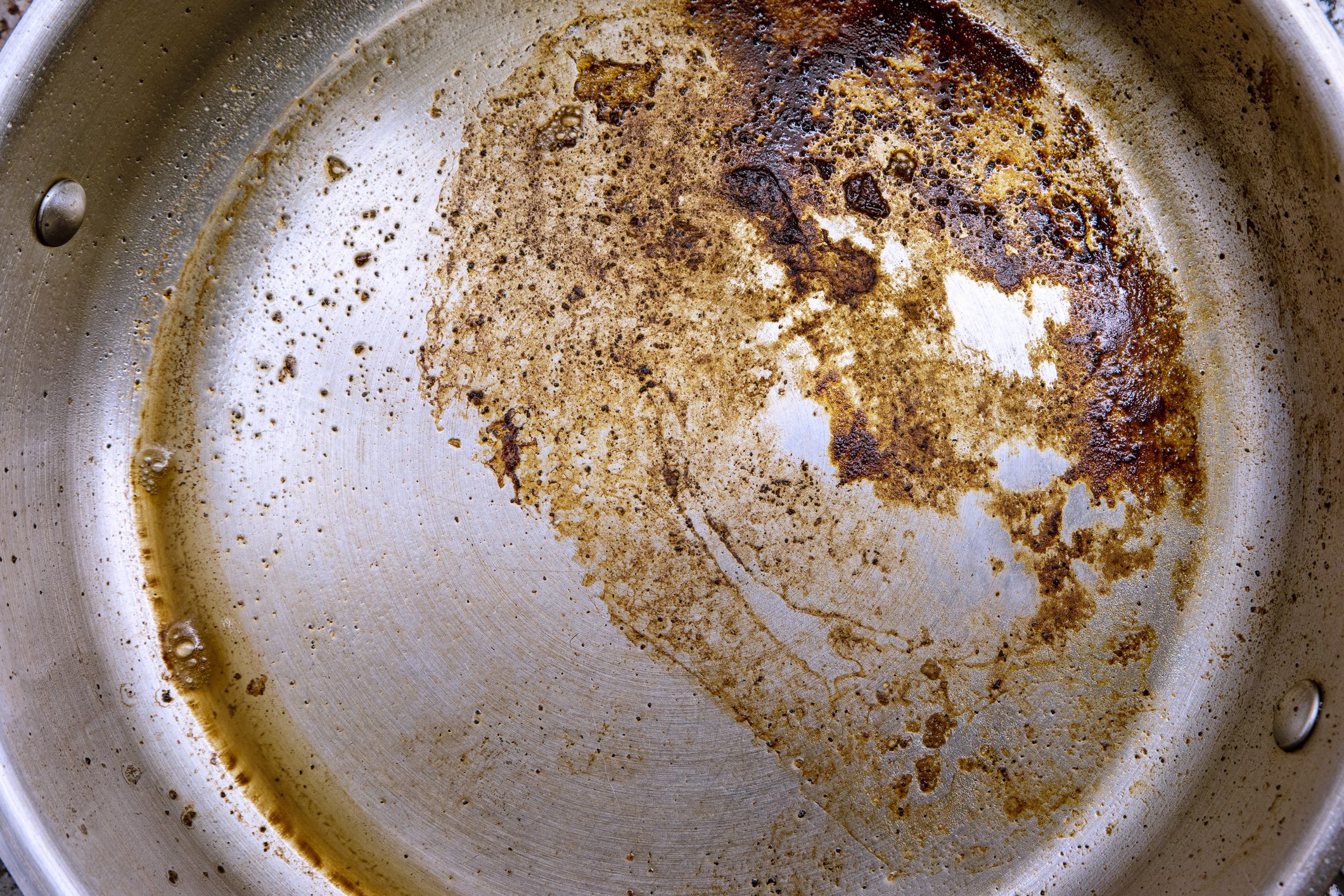 O óleo e a gordura queimados permanecem no fundo de uma frigideira de aço inoxidável, fechando a vista superior.