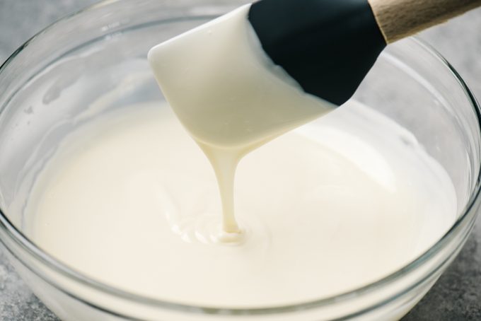 Melted white chocolate dripping from a spatula into a mixing bowl