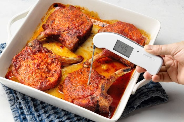 Pork Chops Fully Cooked In 13x9 Baking Dish Being Temperature Tested With Meat Thermometer.