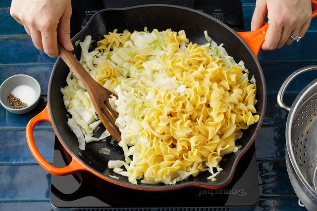 hands Mixing cabbage and noodles Together in an orange skillet