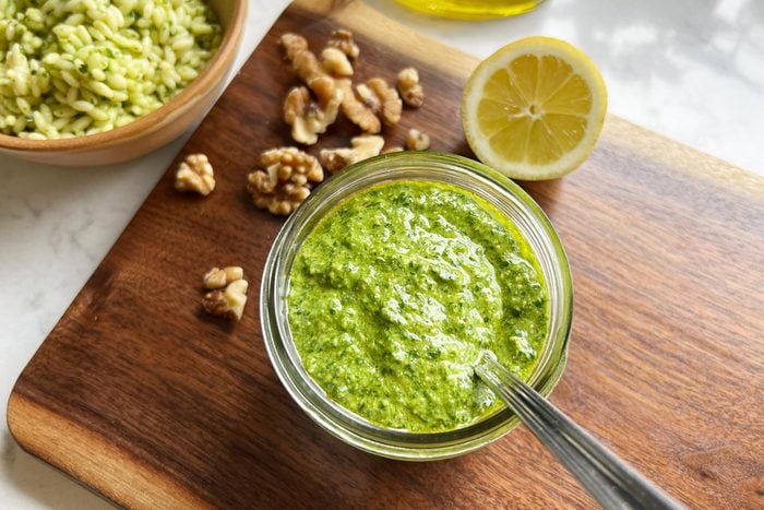 spinach pesto in a small glass dish with a spoon on a wooden cutting board