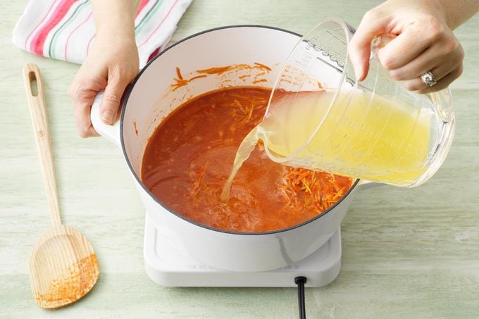 pouring broth into blended tomato soup base