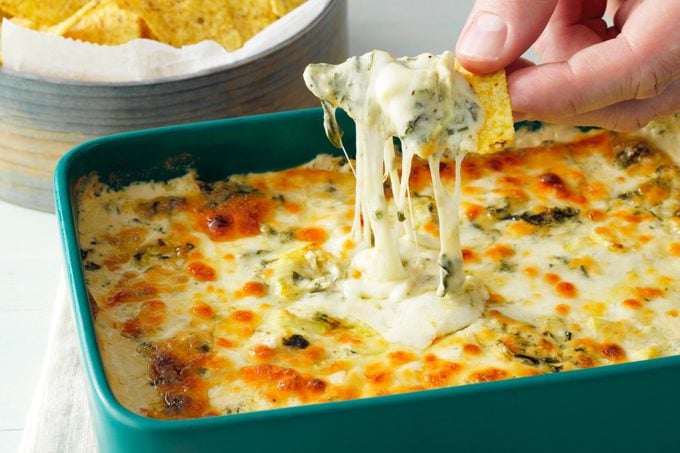 dipping chip into a casserole dish of Copy Cat Applebees Spinach Artichoke dip