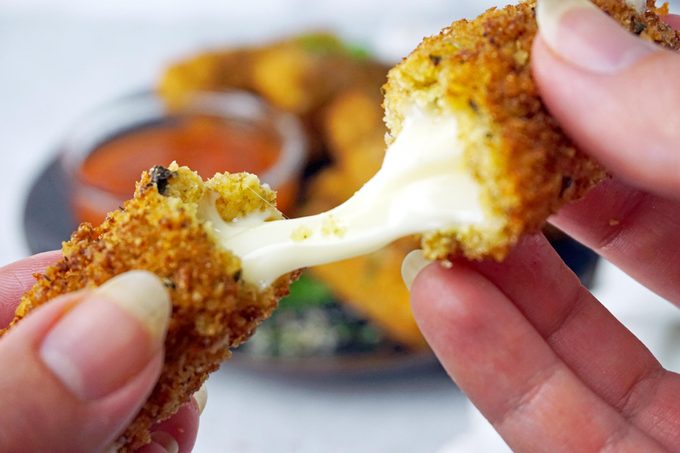 hands breaking a mozzarella stick showing the cheese inside