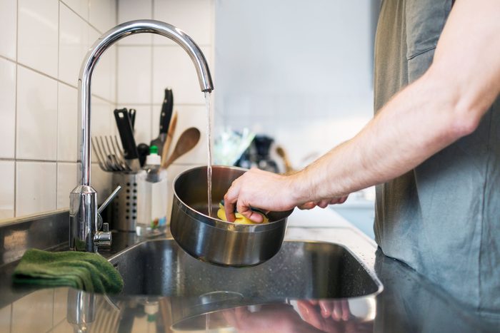 anonymous Man Washing stainless steel sauce pan in the sink at home