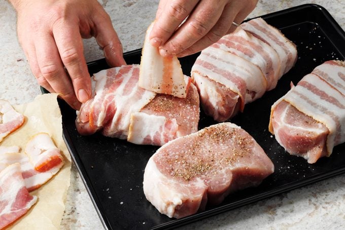 Hands Wrapping Pork Chops With Bacon