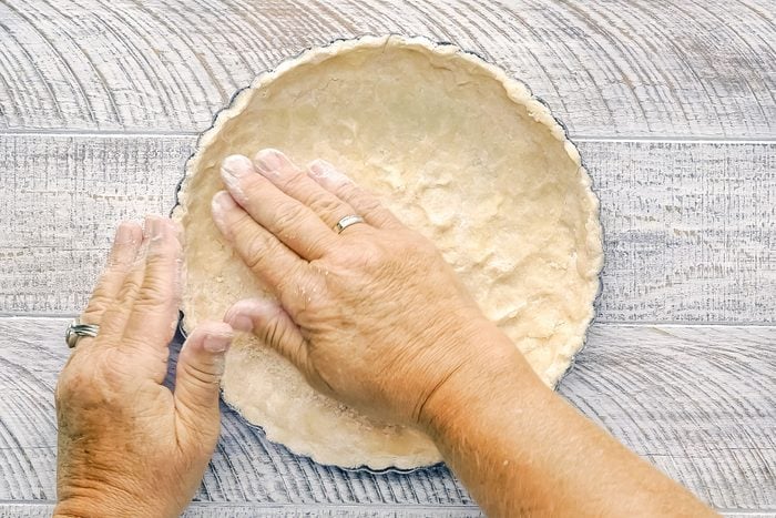 pressing Blueberry Tart dough in tart pan with hands on wooden surface