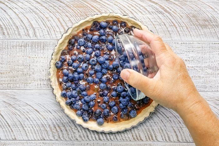 Pouring Blueberry Tart Filling on pressed dough in tart pan on wooden surface