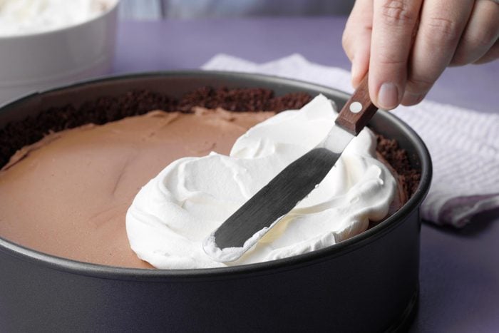 A Person Spreading Whipped Cream Over the Chocolate Filling