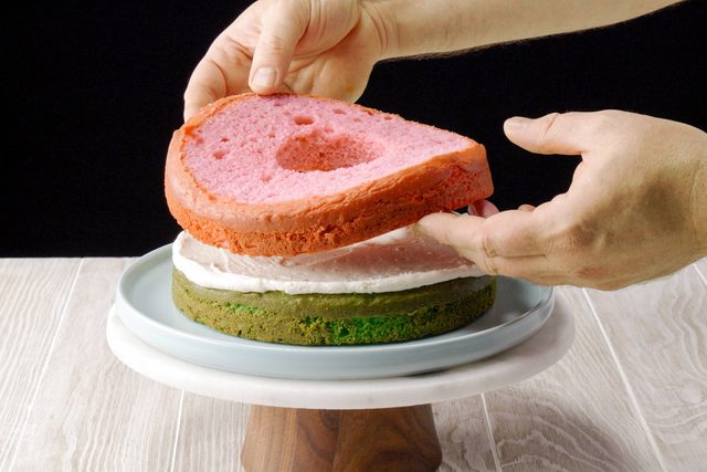 Hands assembling layers of the surprise cake on a cake stand
