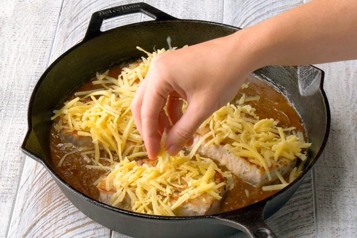 sprinkling cheese on top of the pork chops in a cast iron skillet