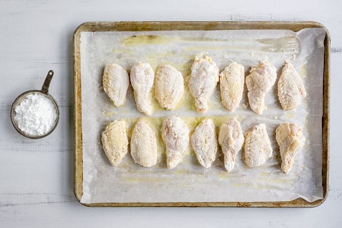 Baking Powder Coated Chicken Wings on Baking Sheet and Baking Plate on Wooden Surface with Baking Powder in Mini Bowl