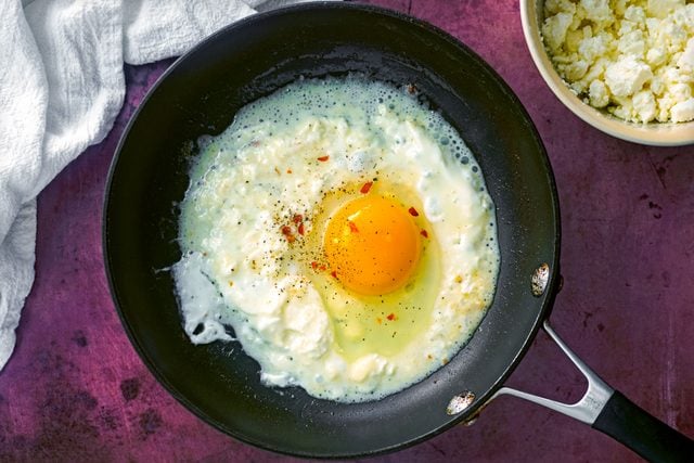 frying an egg in a skillet with feta cheese crumbles