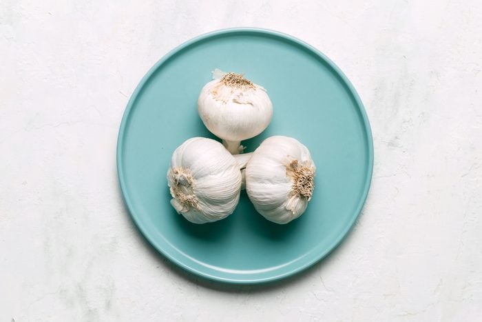three Garlic cloves on a turquoise colored plate on a white counter top