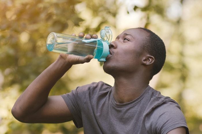 Young Black Man Drinking Water From Sport Bottle At Park
