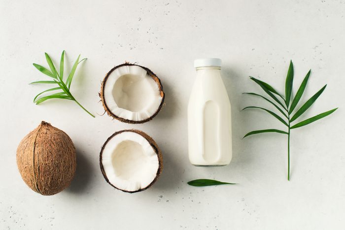 Coconut milk in glass bottle with coconuts on white