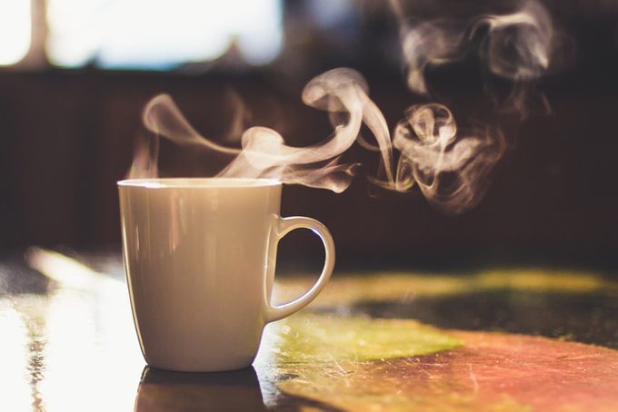 Close up of steaming cup of coffee or tea on vintage table in the early morning on a rustic background