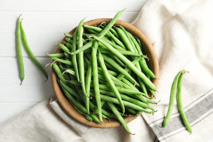 raw green beans in a wood bowl on a white wood table with a towel to the side