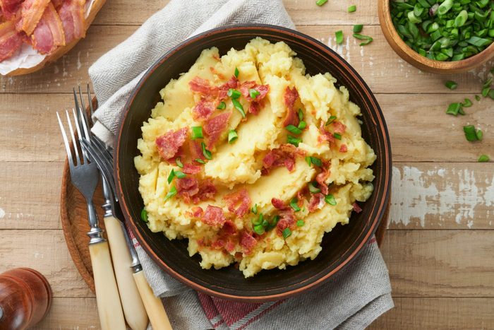 Mashed potatoes with bacon, green onion, pepper and cheddar cheese in bowl on old wooden background