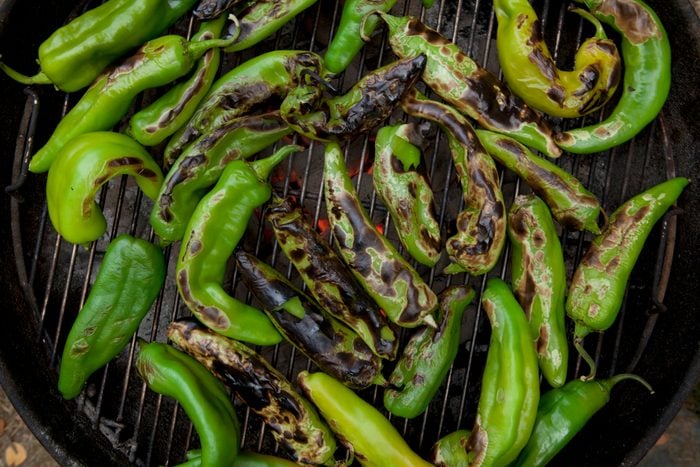 Hatch Chiles roasting over a fire on top of grill grates