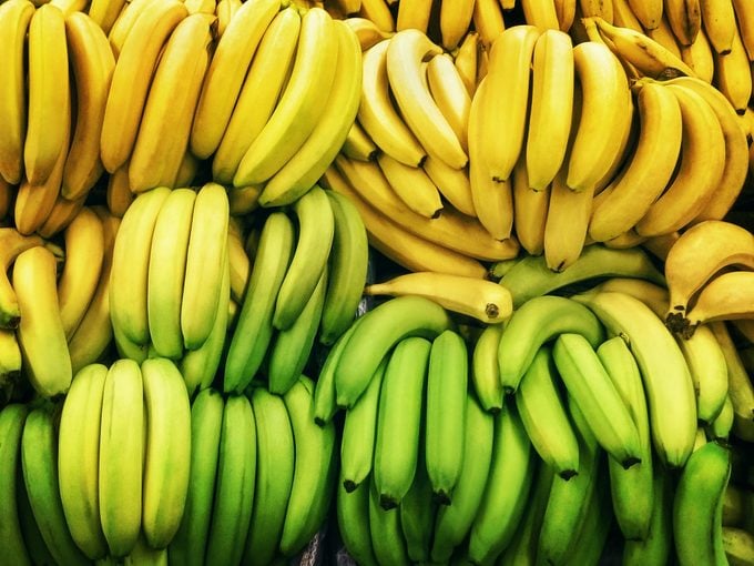 Green and ripe yellow bananas are lying in rows on the market Top view