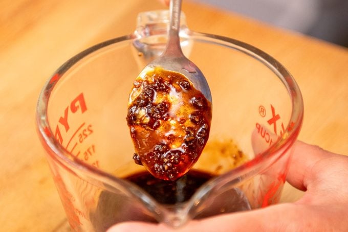 Sauce on a Spoon and Glass Jar on Wooden Surface