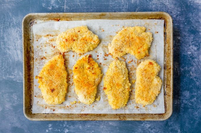 Baking sheet with baked breaded chicken breast cutlets on blue surface