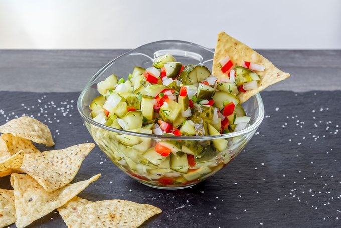 Glass bowl of chopped pickle de gallo with tortilla chips on stone surface