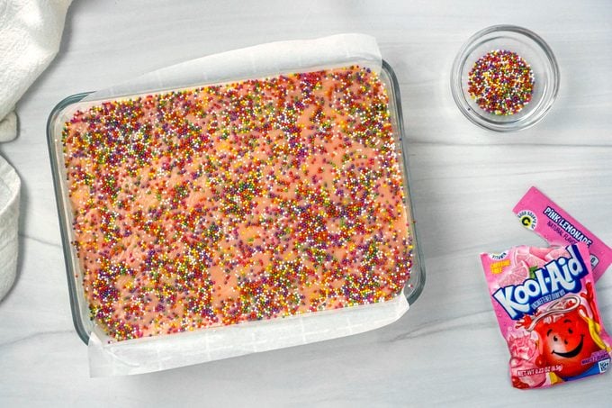 A Glass Dish with Pink Lemonade Fudge Topped with Rainbow Sprinkles ready to be cut into Cubes