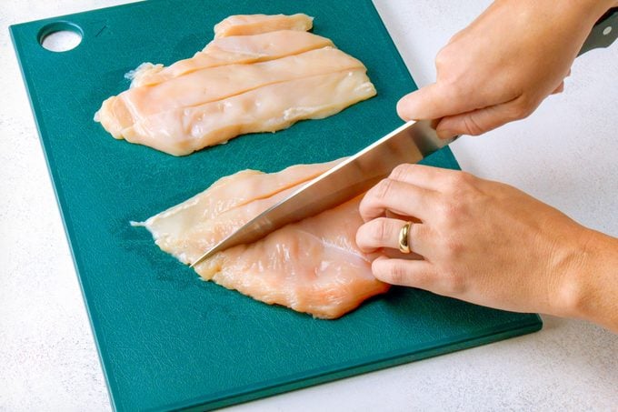Cutting Chicken into Pieces on Cutting Board with Knife