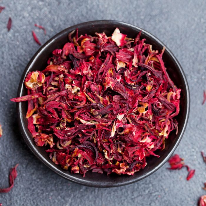 Hibiscus flower tea in black bowl on grey stone background. Copy space. Top view.