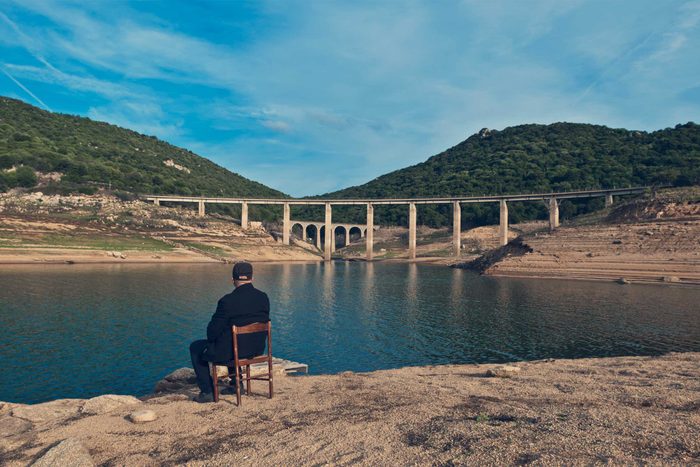 An old man sitting in a chair looking at a lake in Sardinia