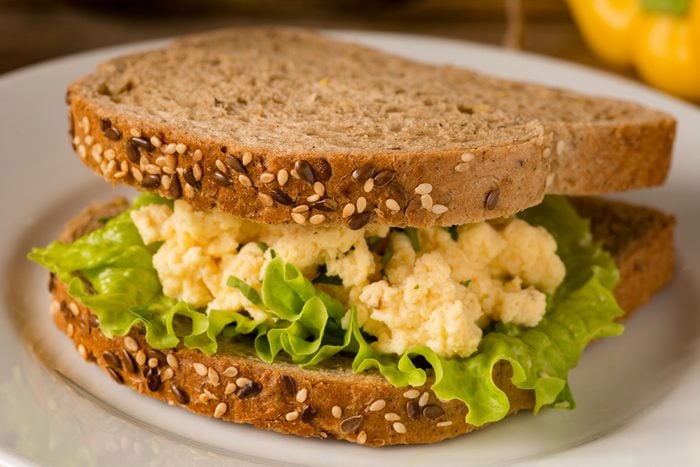 Egg salad Sandwich with scrambled eggs and green lettuce salad on white plate