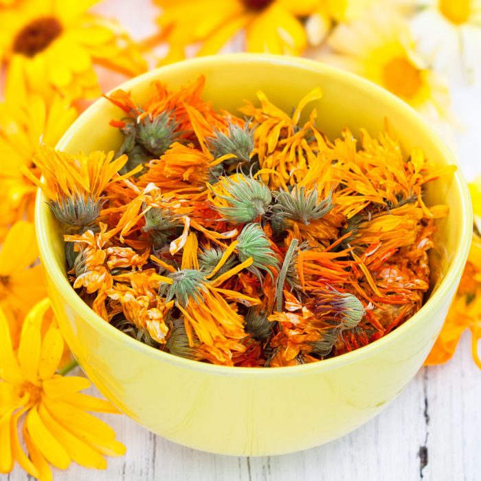 Fresh and dried calendula flowers on white wooden background