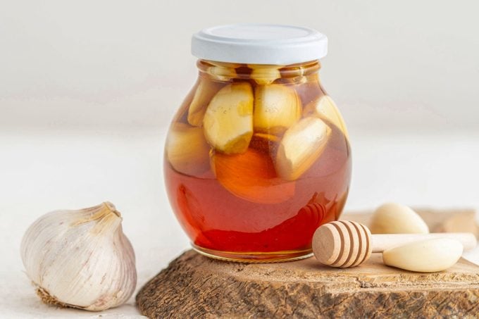 Jar Of Honey With Garlic Inside And A Honeycomb, On A White Background, Home Remedy For Flu